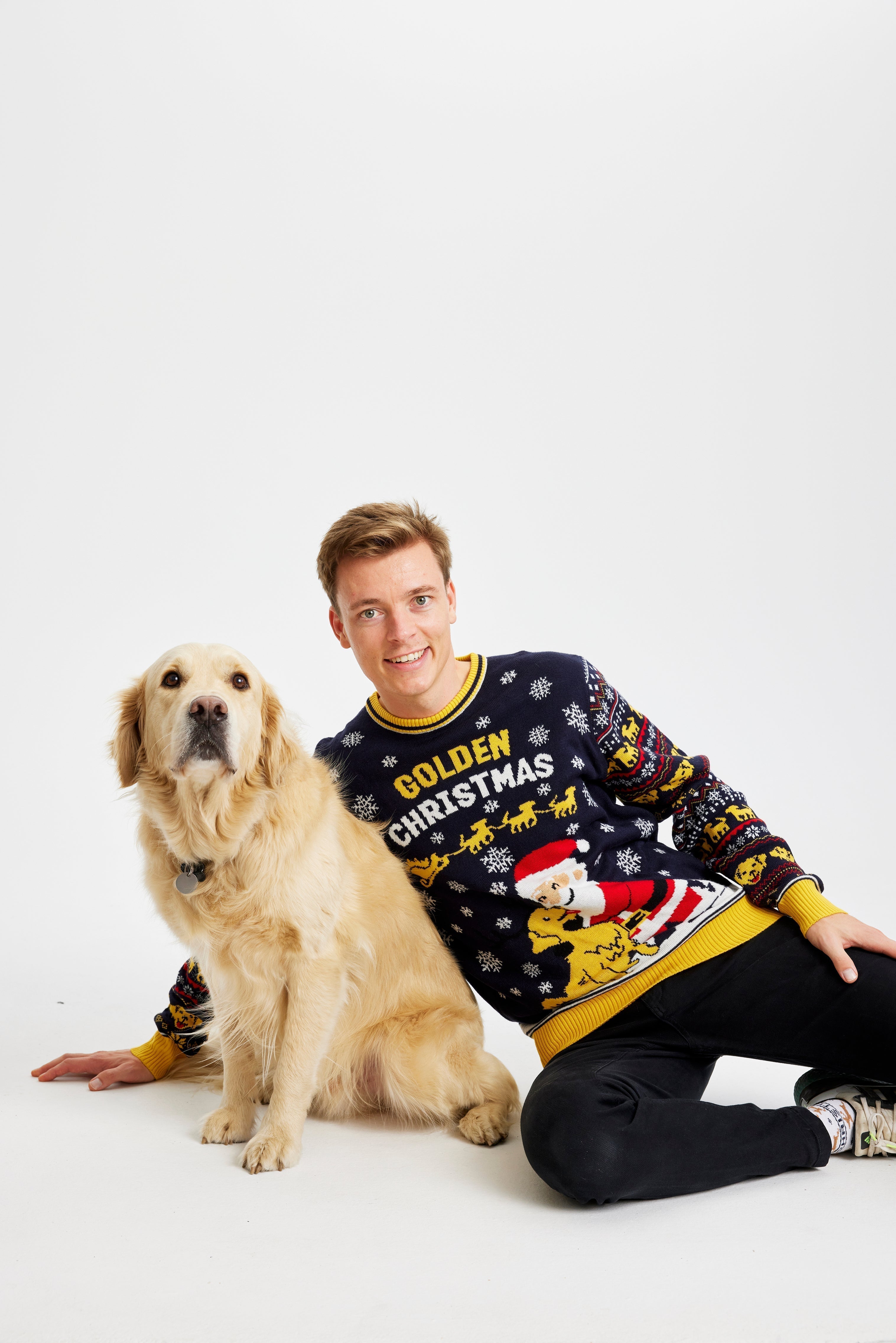 Un homme souriant pose avec un chien vêtu d'un pull de Noël jaune et noir portant l'inscription